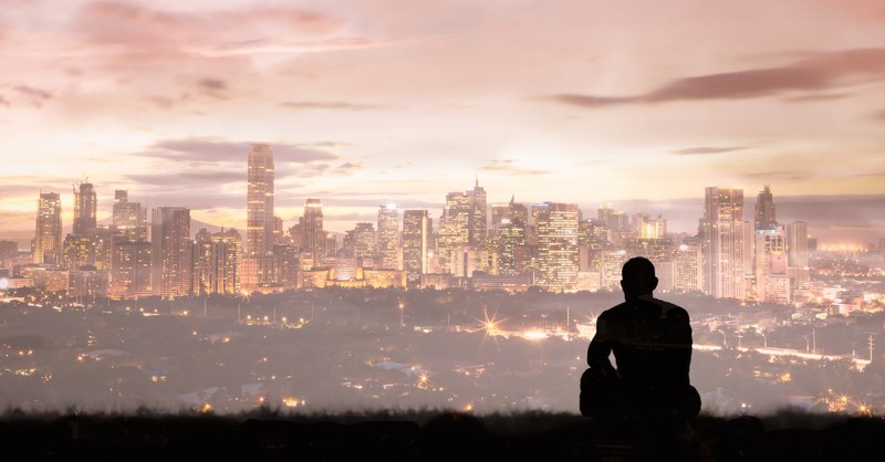 Silhouette of a man sitting alone, looking out at a city