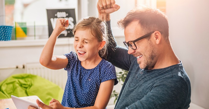 dad and young daughter fist pump celebrate in front of computer