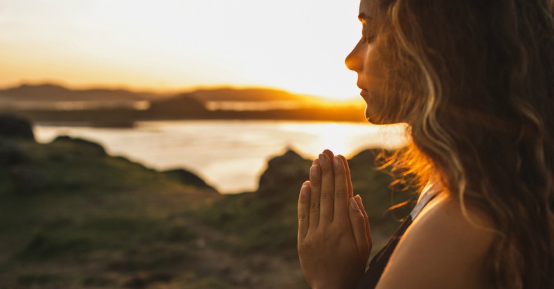 woman praying outside at sunset by river