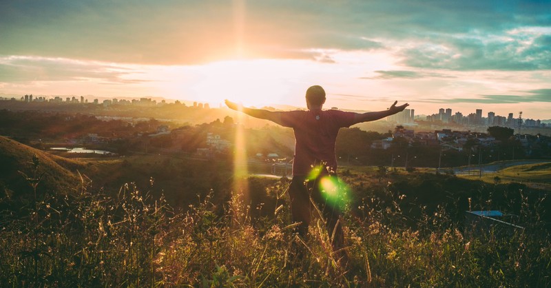 Man standing at sunset with arms out