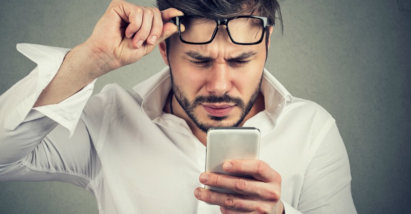 man strains his eyes looking at cell phone 