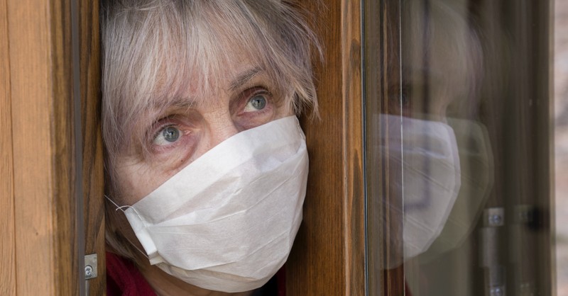 elderly woman in face mask for COVID-19 peering out her front door