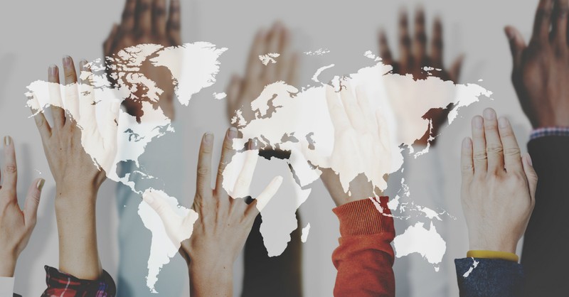 multicultural hands raised behind overlay of world map