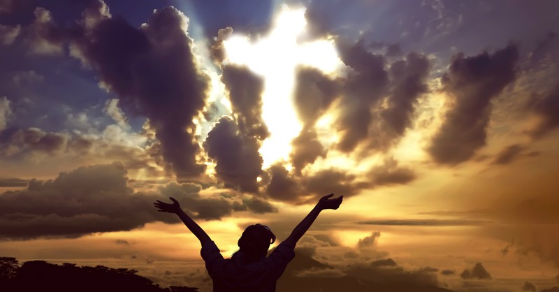 woman with arms up in praise toward cross breaking through clouds