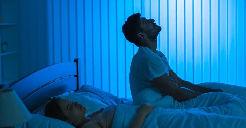 man sitting up in bed looking restless and worried