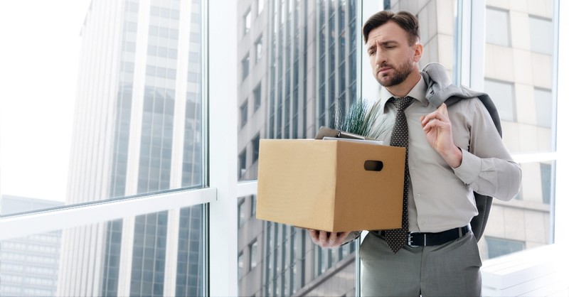 Sad man fired from his job, carrying a box out of the office