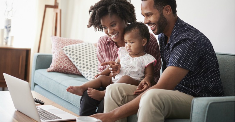 man and wife sitting with baby on couch in front of computer, pray for pasto