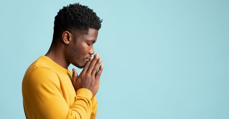 Young man with hands folded and eyes closed in prayer