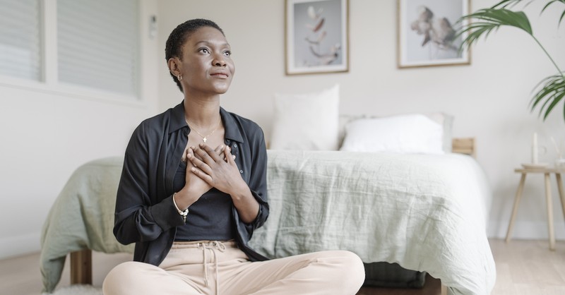 pious woman sitting on floor with hands crossed at chest looking out in prayer