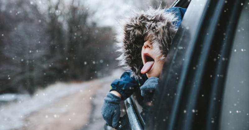 Boy leaning out of a car window, catching snowflakes on his tongue