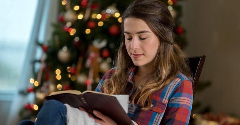 woman praying at Christmas time holding Bible with tree in background