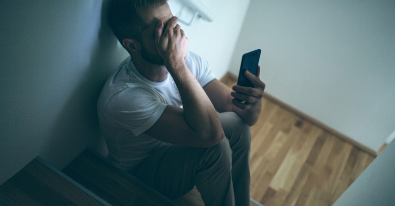 Man depressed on the stairs looking at his phone