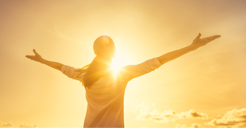 Woman looking up at the sunrise with arms outstretched.