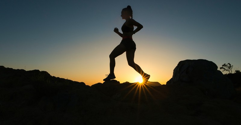 Silhouette of a woman running on a mountain at sunset