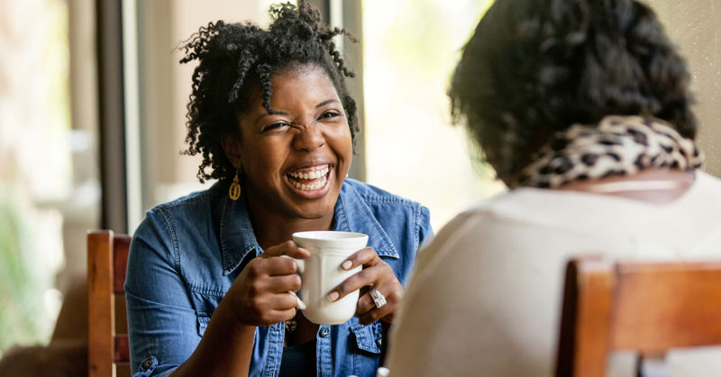 Two friends (women) laughing over coffee.