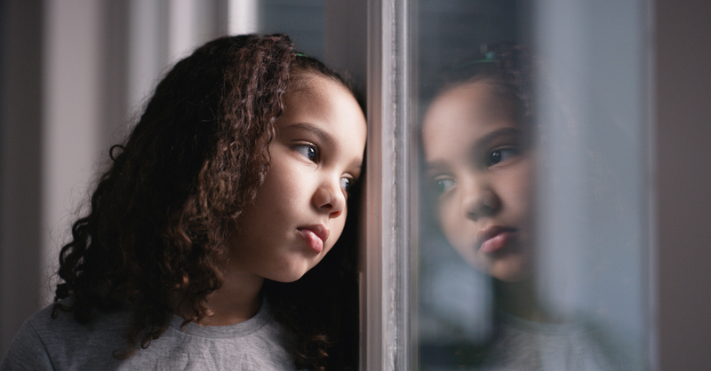 Grieving, traumatized little girl looking out the window sadly.