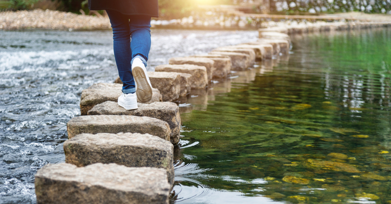 Person hiking across water on stones; a prayer for discerning God's directions.