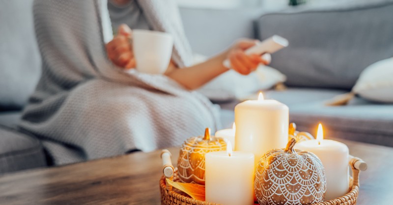 Woman with mug and TV remote watching show or movie in fall candles