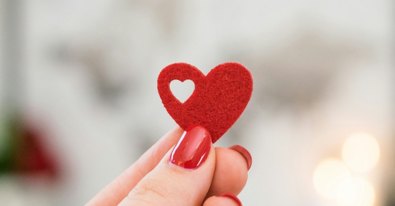 red fingernails holding up a heart with a heart cut out