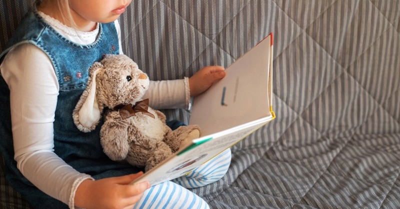child reading storybook with toy rabbit
