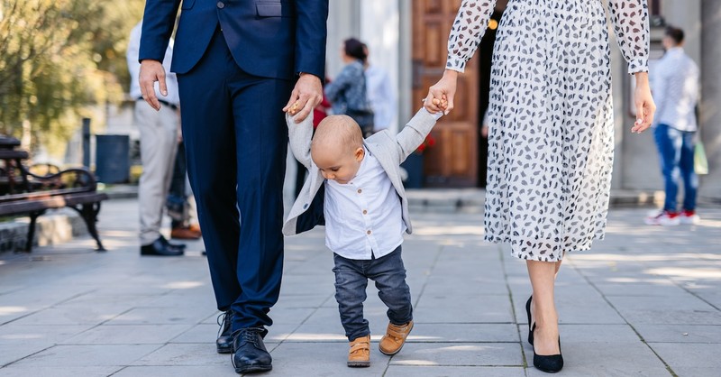father and mother holding toddler's hands as they walk from church