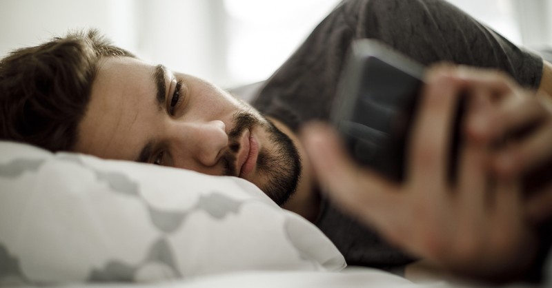 Man checking cell phone in bed in morning