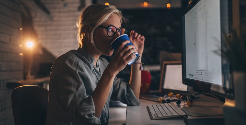 Woman working late in office at job at night drinking coffee