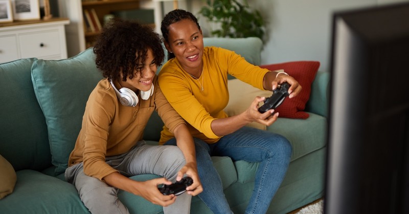 Mother and teen son playing video game together on couch gaming