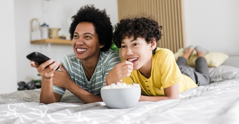 Mother and teen son on bed with popcorn movie night remote