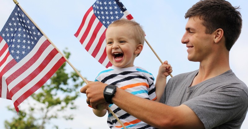 Dad holding young son and American flags on the 4th of July