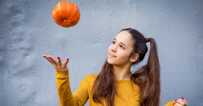 young girl tossing pumpkin into air