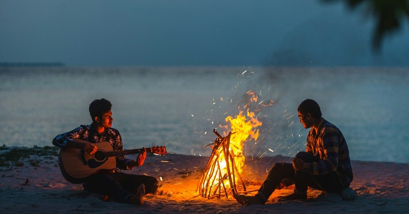 Two men sitting by a bonfire on the beach