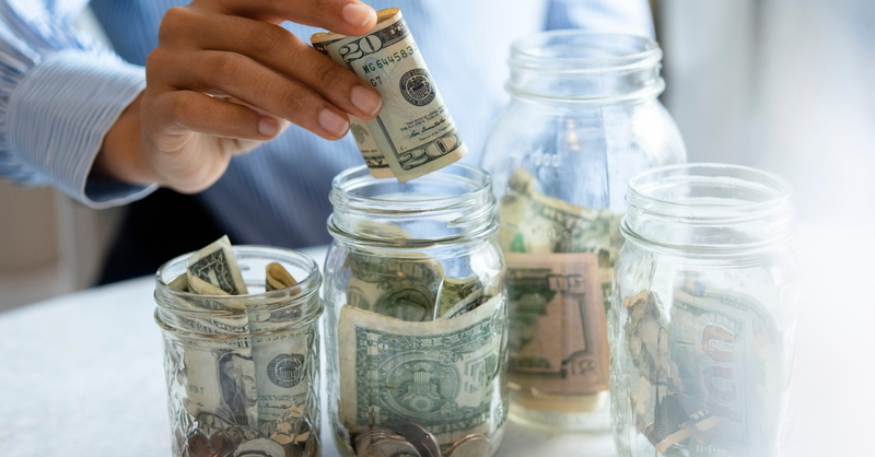 hand putting money in savings jar labeled savings