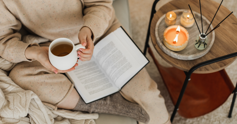 Someone wrapped in a blanket sipping tea by candlelight