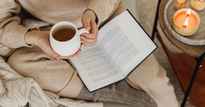 Woman reading book open Bible and tea in mug cozy fall quiet time