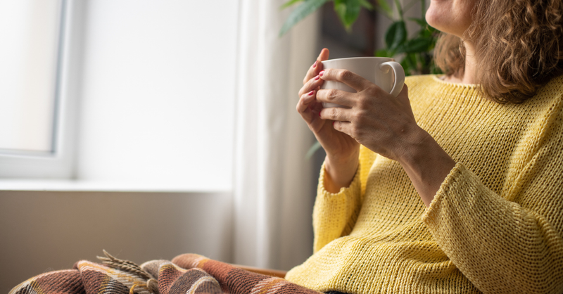 Woman wrapped in blanket with warm drink by window