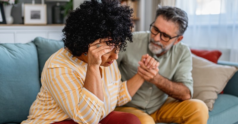 Husband supporting crying stressed wife on couch married couple