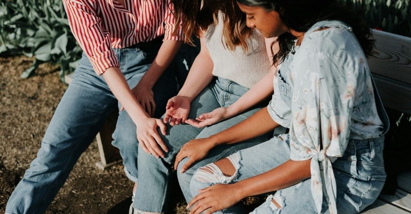 Three women sit together on a park bench, offering comfort and support as they talk and listen, illustrating friendship, encouragement, and Christian community.