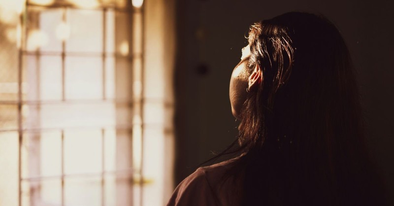 A contemplative photograph of a woman gazing toward sunlight streaming through a window, her face illuminated by the warm light, symbolizing hope, prayer, God's presence, and the quiet assurance of His faithfulness.