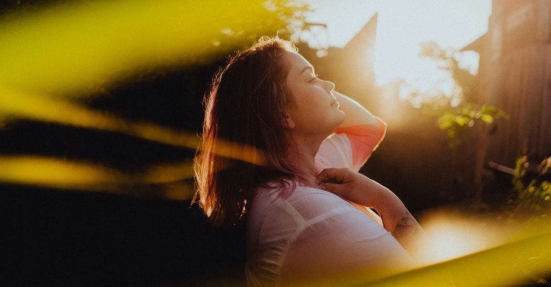 A peaceful image of a woman with her eyes closed, basking in warm golden sunlight outdoors, conveying gratitude, freedom, renewal, and the joy of resting in God's presence.