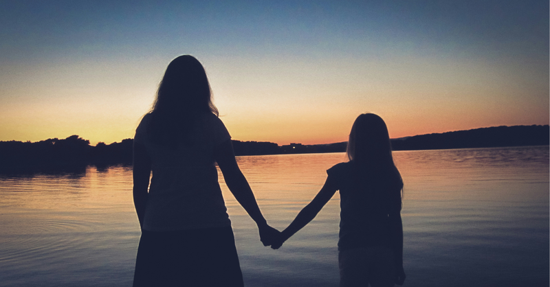 A mother and daughter hold hands while watching a peaceful sunset over a lake, symbolizing trusting God with a child's future, walking together in faith, and finding hope in His faithful guidance.
