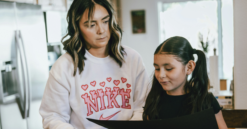 A mother and young daughter look at a paper together in their kitchen, representing intentional parenting, teaching children God's truth, and encouraging faith-filled conversations at home.