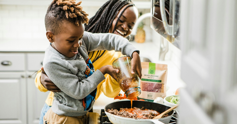 Mother and young son smiling as they cook a meal together in the kitchen.