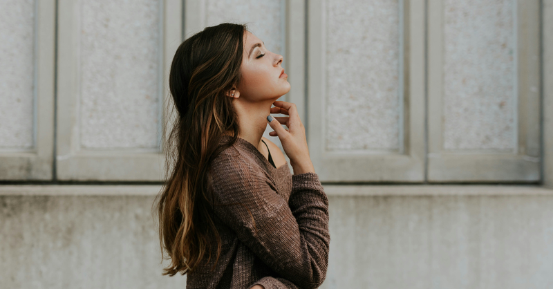 Woman standing outdoors with her eyes closed in a quiet moment of reflection and prayer.