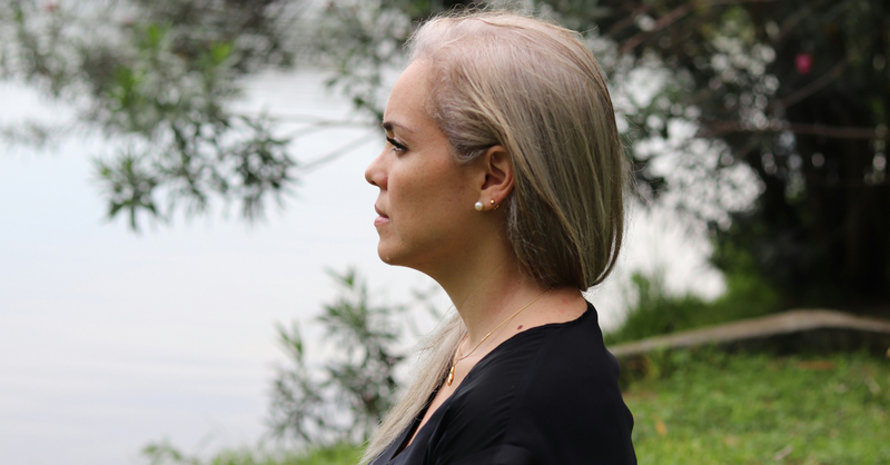 Woman with gray hair gazes thoughtfully across a peaceful lake while spending time outdoors in quiet reflection.