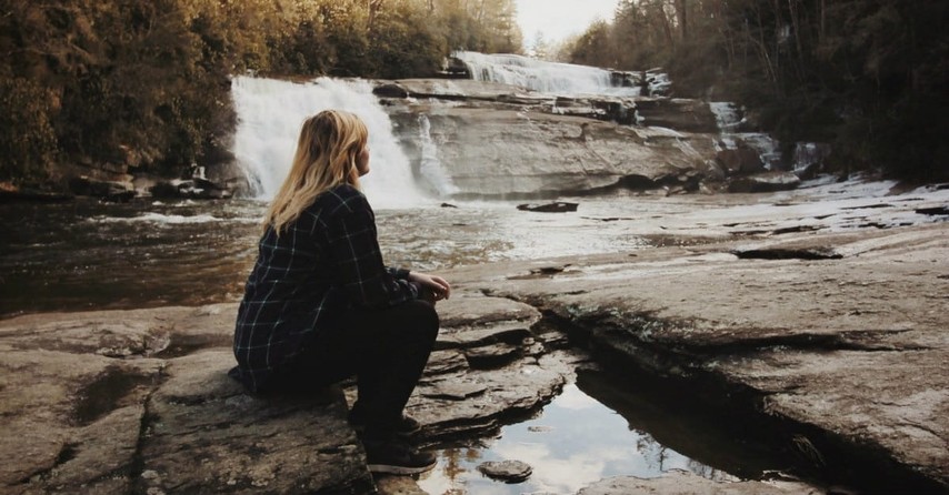 sad woman sitting by stream, comforting bible verses about grief and loss