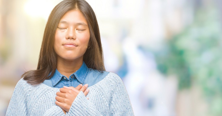 Peaceful woman with eyes closed and hands over her chest