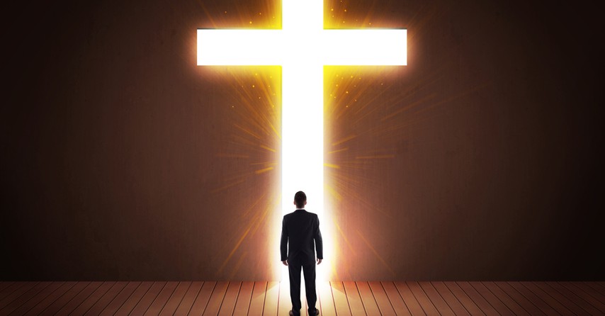 man in suit walking through lit doorway of Jesus cross