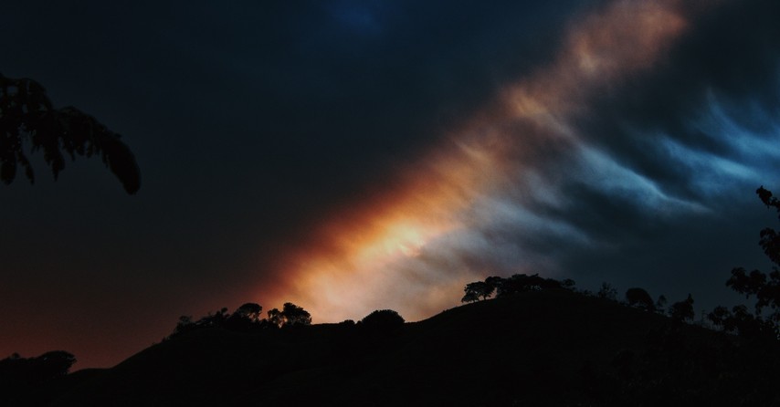 silhouette of hillside with dark clouds and rainbow