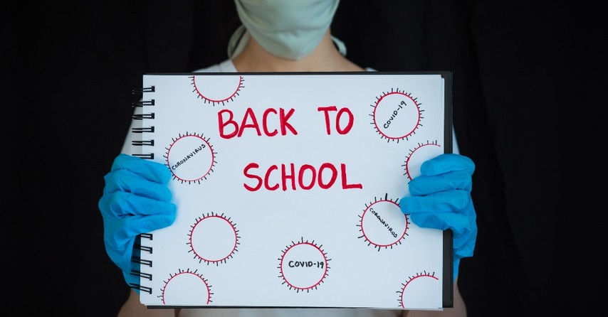 woman in mask and gloves holding up notebook saying covid back to school peace decisions